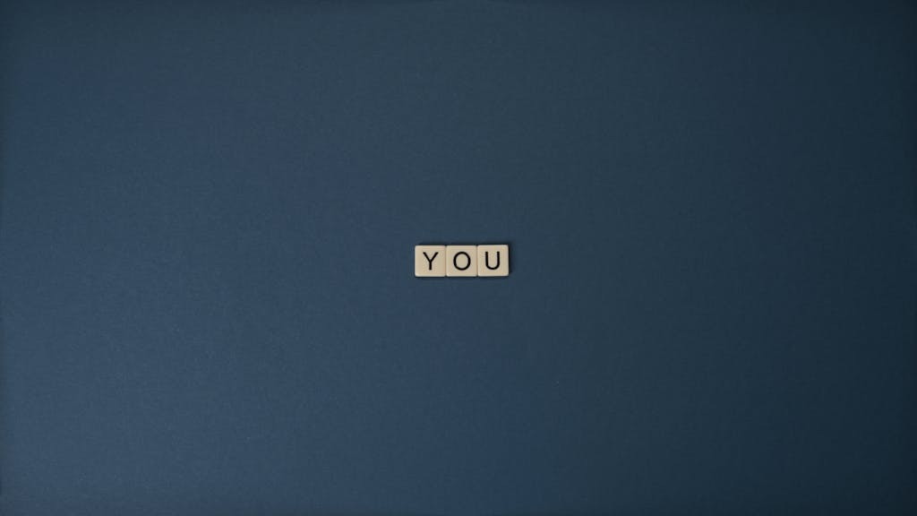 Flat lay of Scrabble letters spelling 'YOU' on a blue background, perfect for conceptual themes.