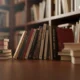 Books neatly arranged on a wooden table in a softly lit library with shelves in the background.