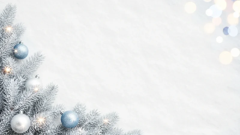Frosted pine branches with blue and silver baubles and soft glowing lights on white background.
