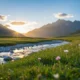Sunset over a mountain valley with a flowing river and wildflowers in the foreground.