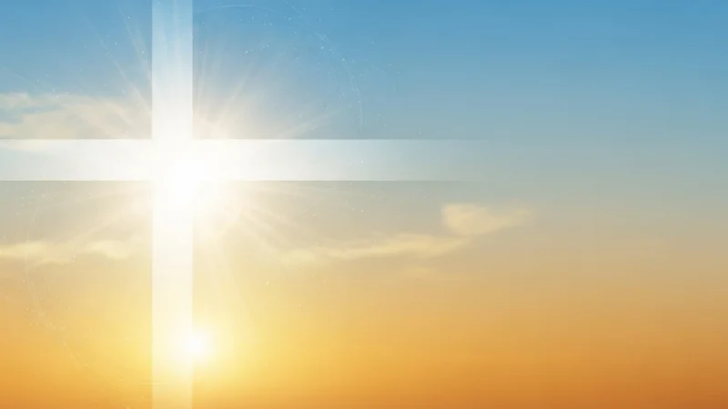 Bright glowing white cross with sun rays against a blue and orange sky at sunrise.