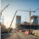 Construction site with cranes, workers in safety gear, and high-rise buildings under development, overlaid with architectural blueprints.