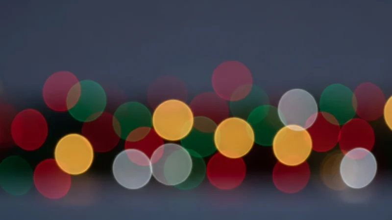 Blurred multicolored circular lights against a dark background, creating a festive bokeh effect.