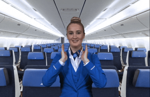 Flight attendant in blue uniform demonstrates safety procedures inside an empty airplane cabin.