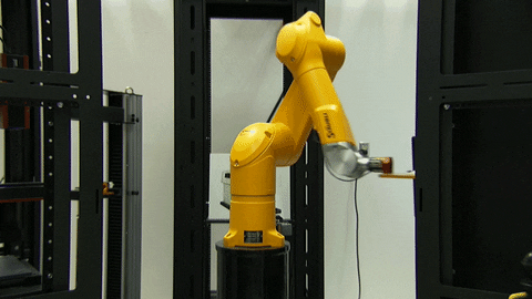 Yellow industrial robotic arm operating in a black metal-framed robotic testing environment.
