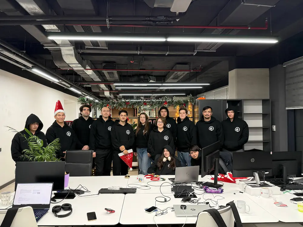 Group of people in black hoodies with a logo posing in a decorated modern office space.