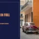 Vintage maroon car parked on a cobblestone street beside orange and peach building facades.