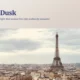 Panoramic view of Paris skyline at dusk featuring the Eiffel Tower under a cloudy sky.