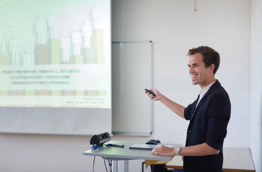 Man in dark blazer giving presentation with projected bar chart on white screen.